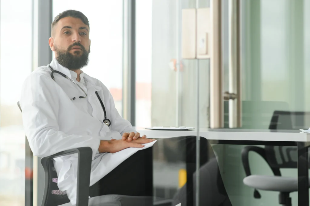 médico com jaleco branco, sentado à mesa de escritório médico